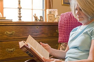 Elderly woman reading a book in her home